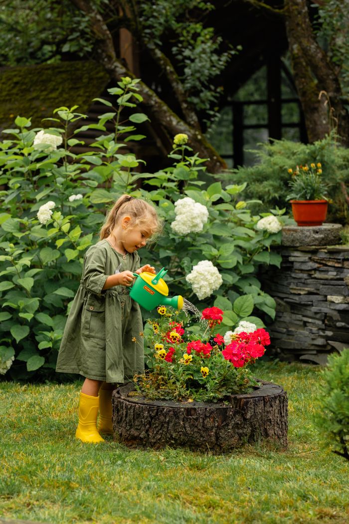 A little girl in a green dress waters vibrant flowers in a lush garden with a cute watering can.